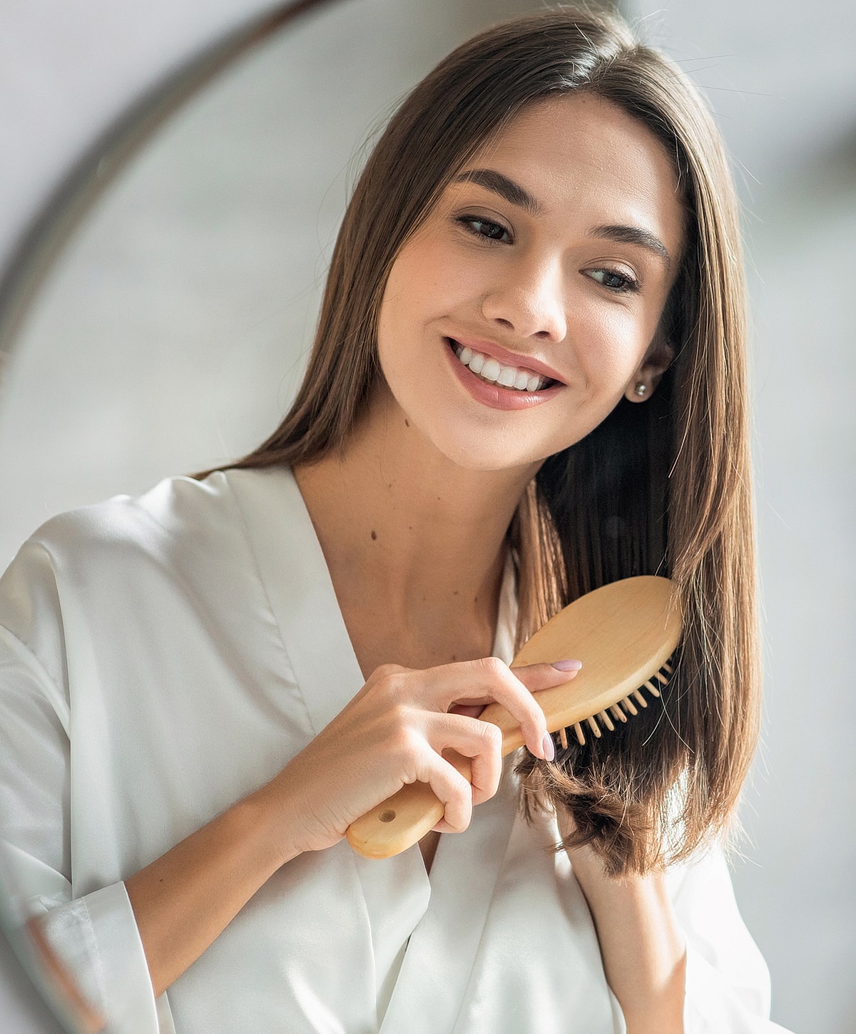 Smiling woman brushing hair in mirror reflection.