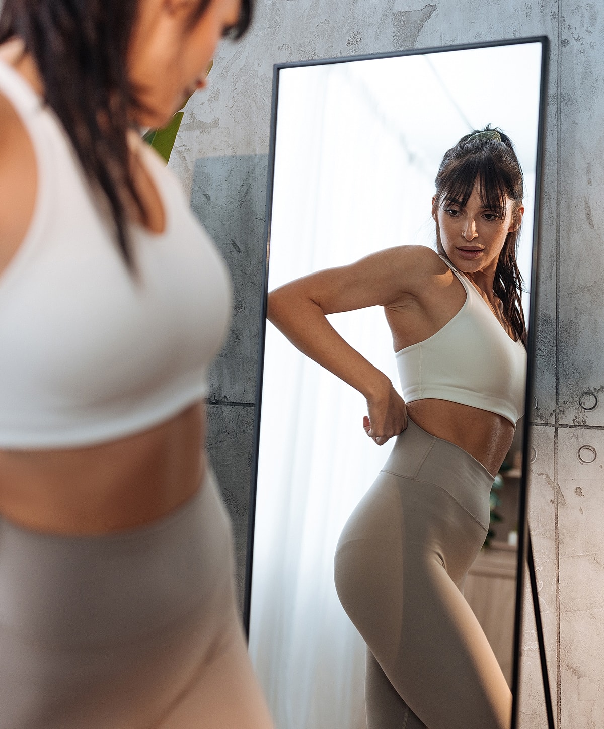 Woman adjusting workout outfit in mirror reflection.