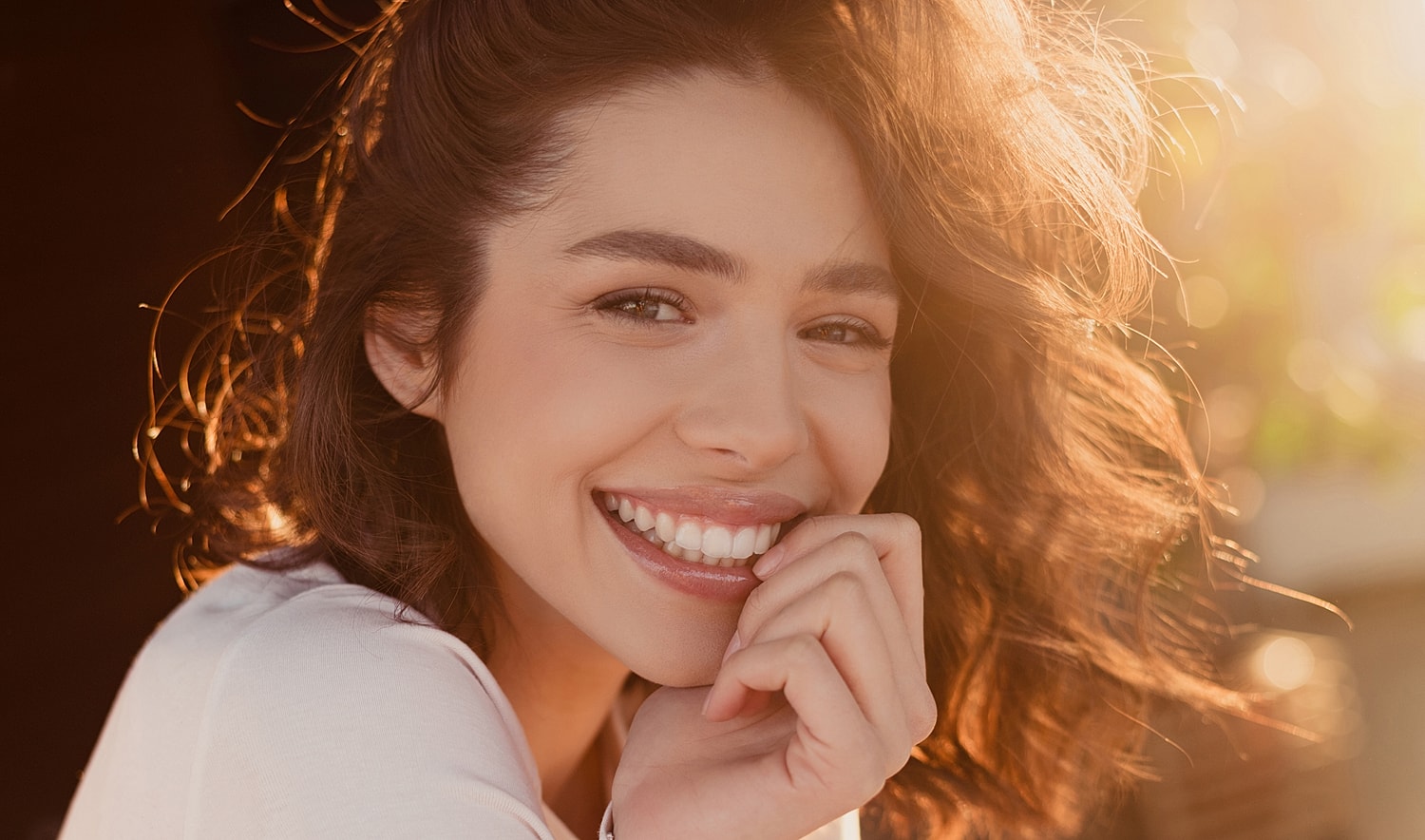 Smiling woman with curly hair in sunlight.