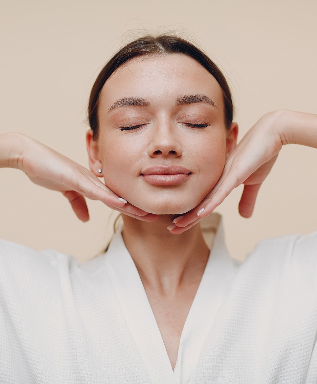 Smiling woman with closed eyes and hands on chin.